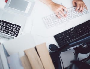 Photo of a person at their desk with a few keyboards and monitors.